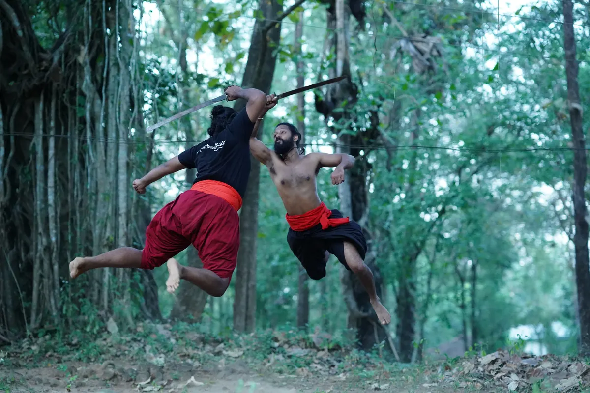 2 students leaping with sticks among the forest trees