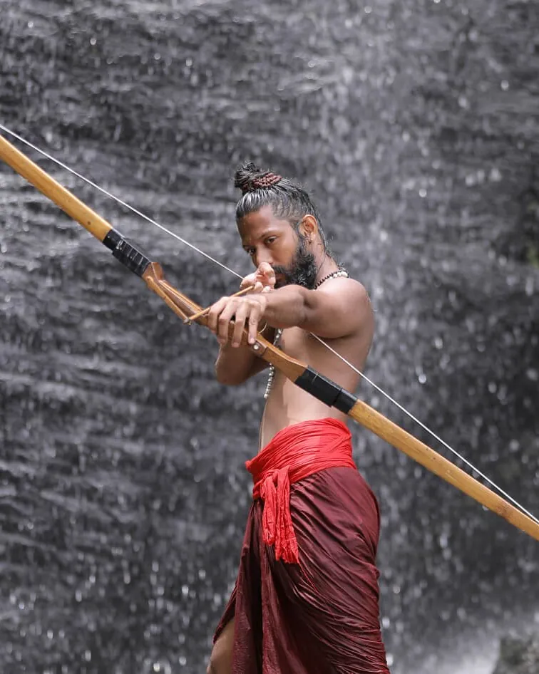Ashan Vipin Das drawing a bow in front of a waterfall