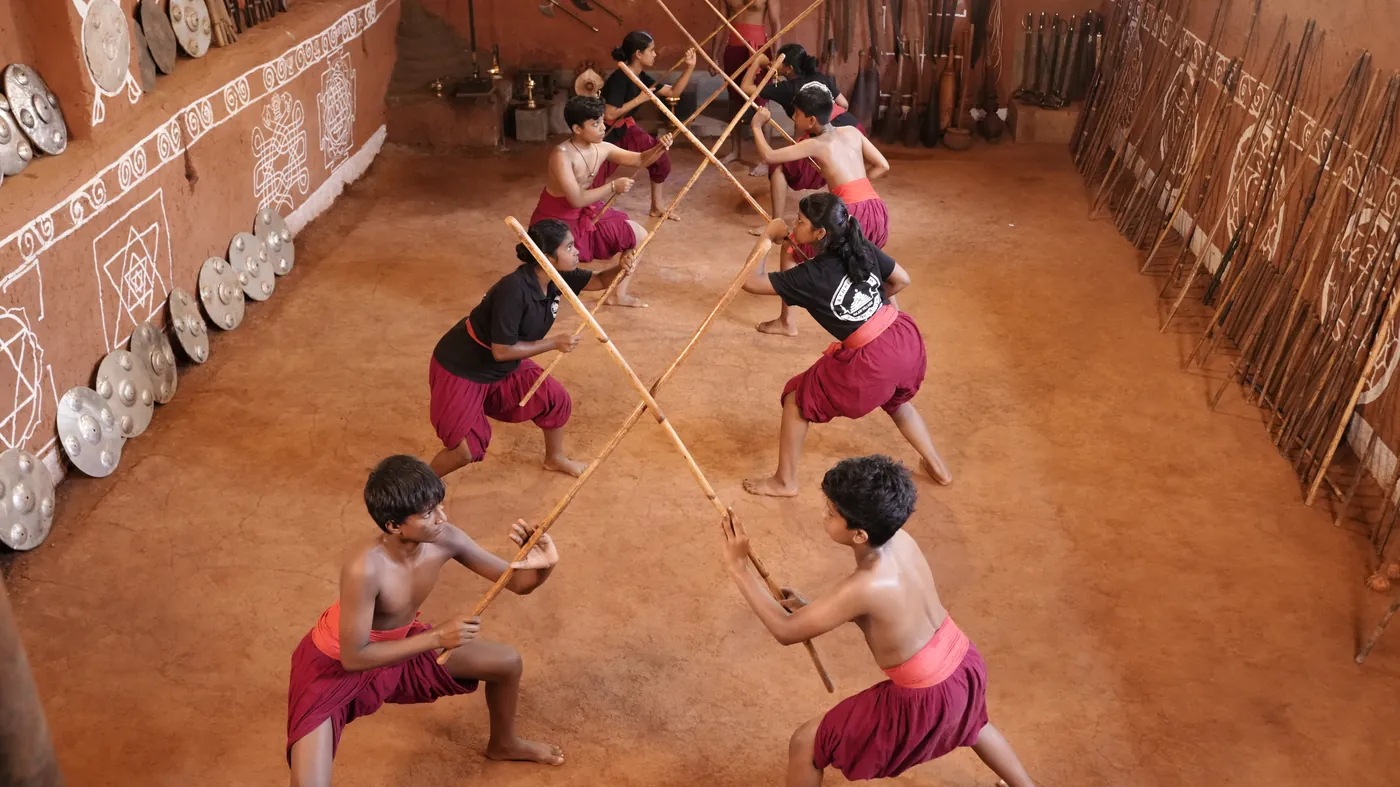 2 Kalaripayattu students crossing long sticks in the kalari