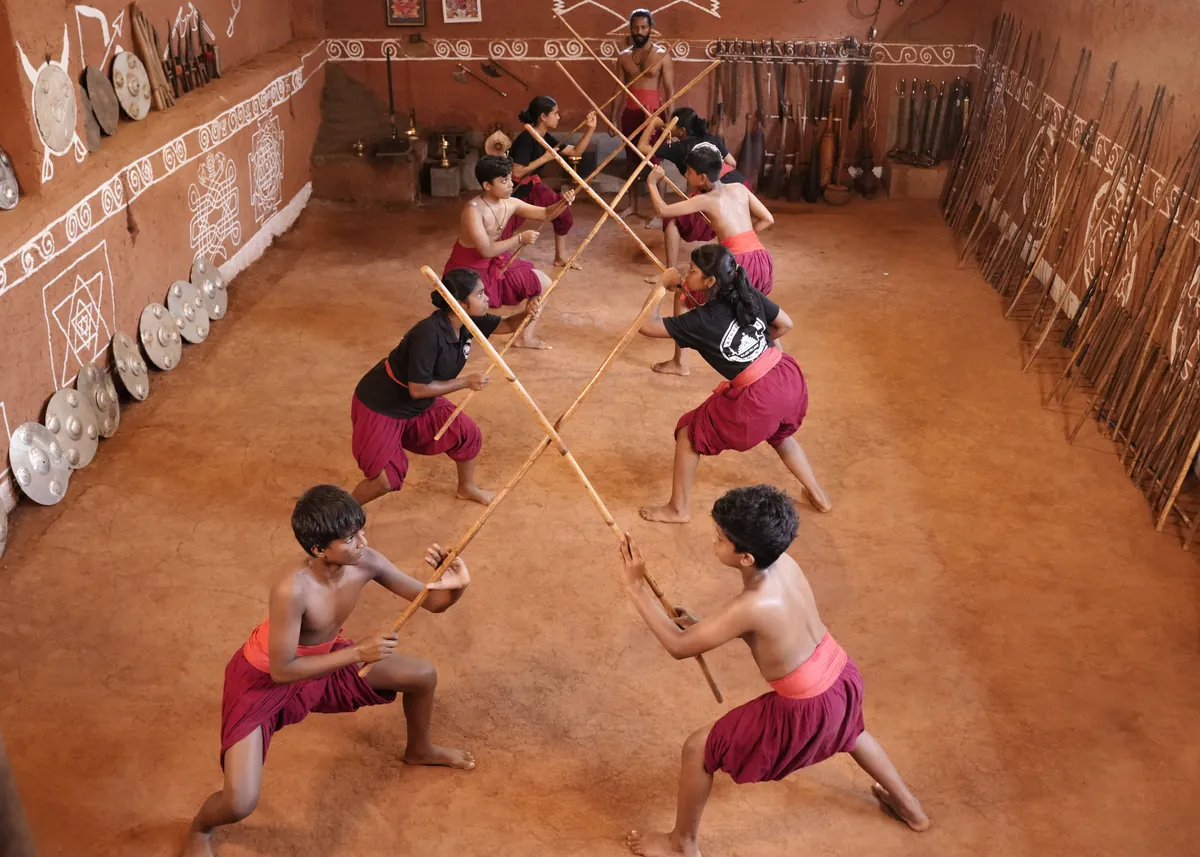 Students practising with long sticks in pairs in the kalari pit